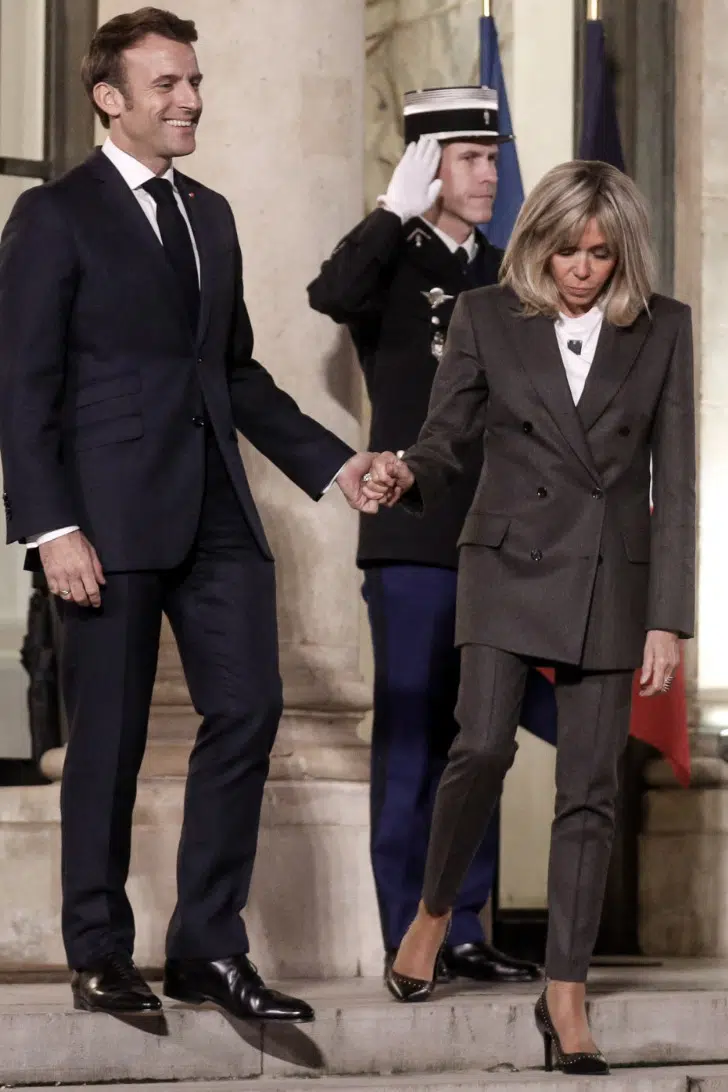 Брижит Макрон в строгом костюме и классической обуви держит мужа за руку