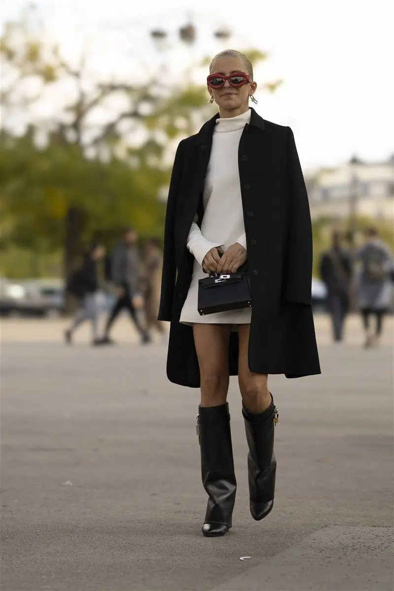 Девушка в белом свободном мини платье, черном классическом пальто и высоких сапогах