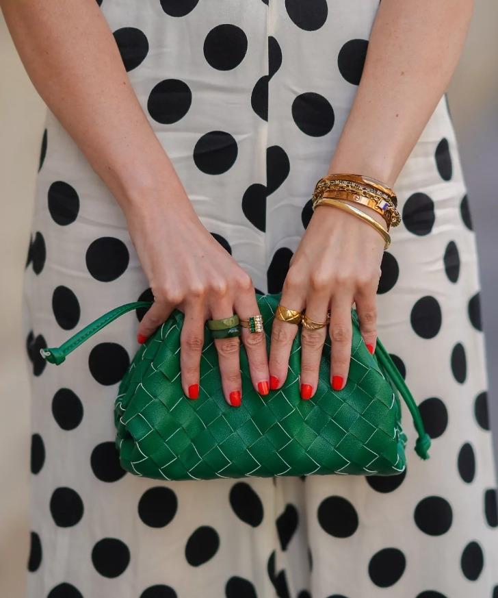 Красный маникюр на коротких ногтях на фоне зеленой сумки