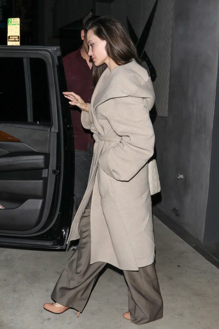 Анджелина Джоли в бежевом пальто с капюшоном и коричневых брюках в пол