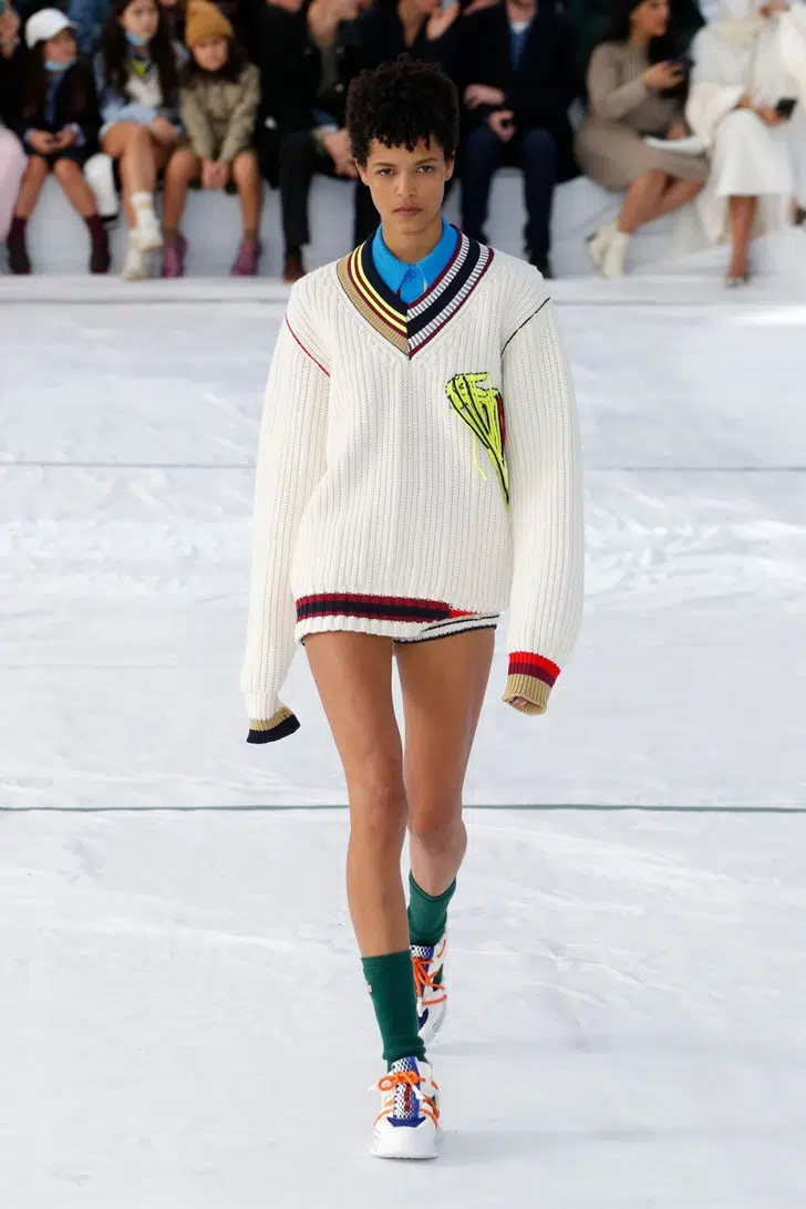Модель в бежевом свитере оверсайз с яркими акцентами от Lacoste