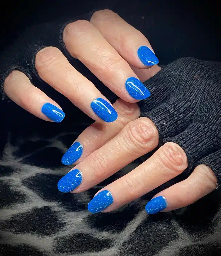 Яркий голубой маникюр с блестками на ухоженных ногтях средней длины
