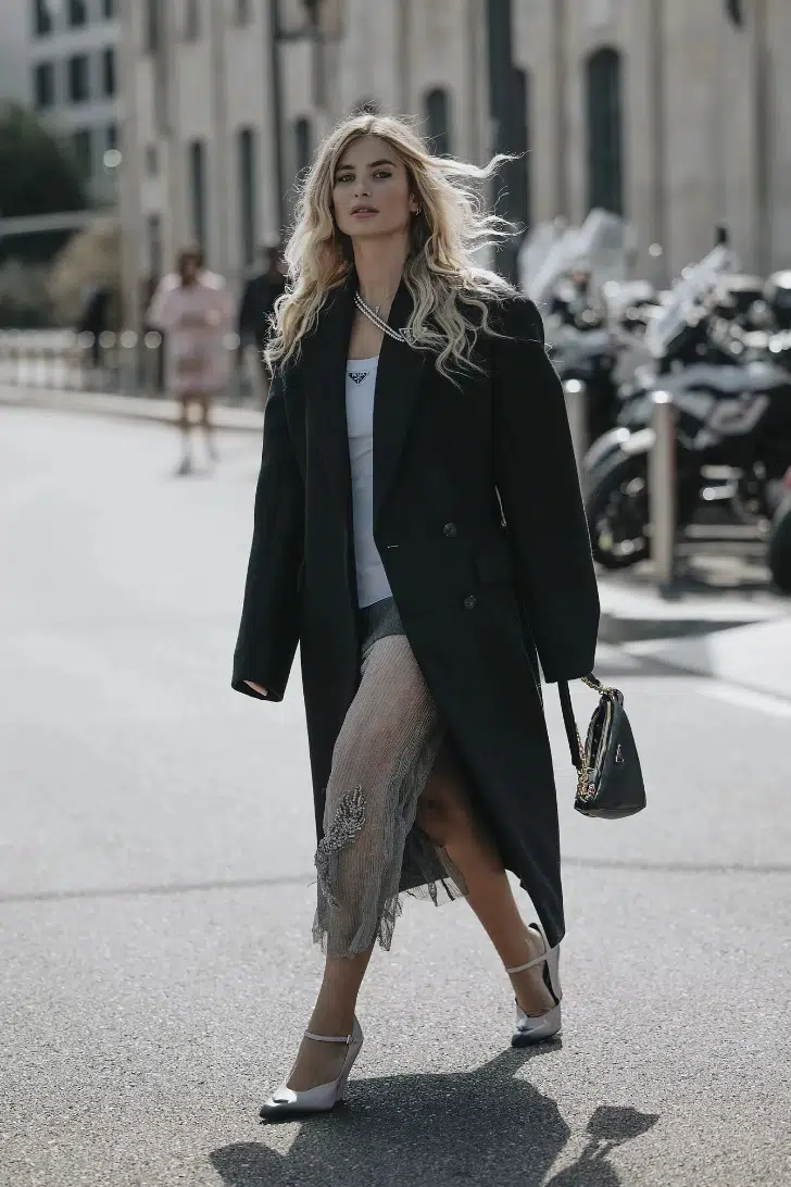 Девушка в миди юбке из прозрачной ткани, черном пальто оверсайз и туфлях на ремешках