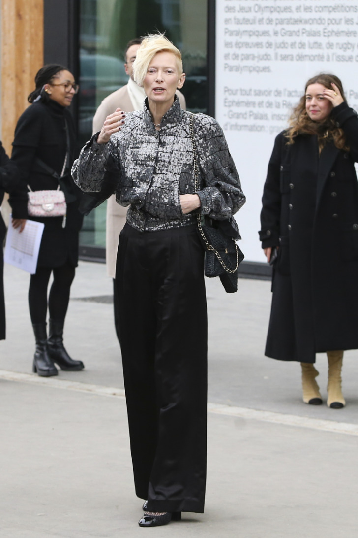Тильда Суинтон в широких черных брюках и укороченной серебристой куртке перед показом Девушка в широких джинсах и черном строгом жакете перед показом Chanel 2023 2023
