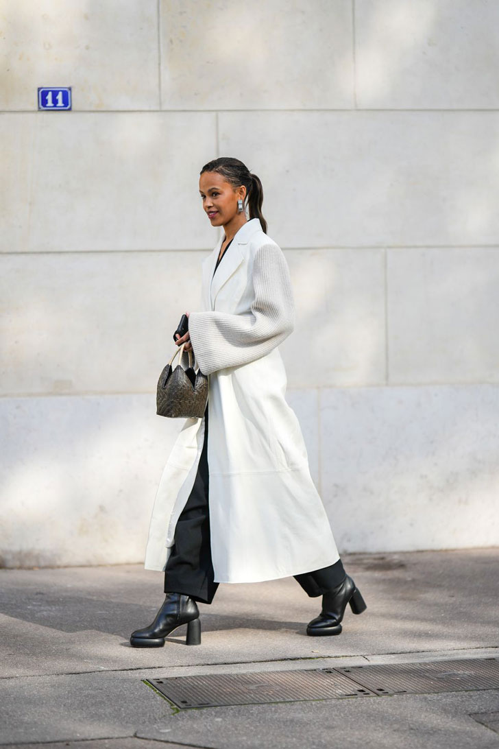 Девушка в белом пальто с вязаными рукавами и ботильонах на каблуке
