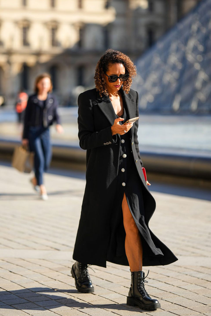 Девушка в длинном черном пальто женственного силуэта и черных ботинках на толстой подошве