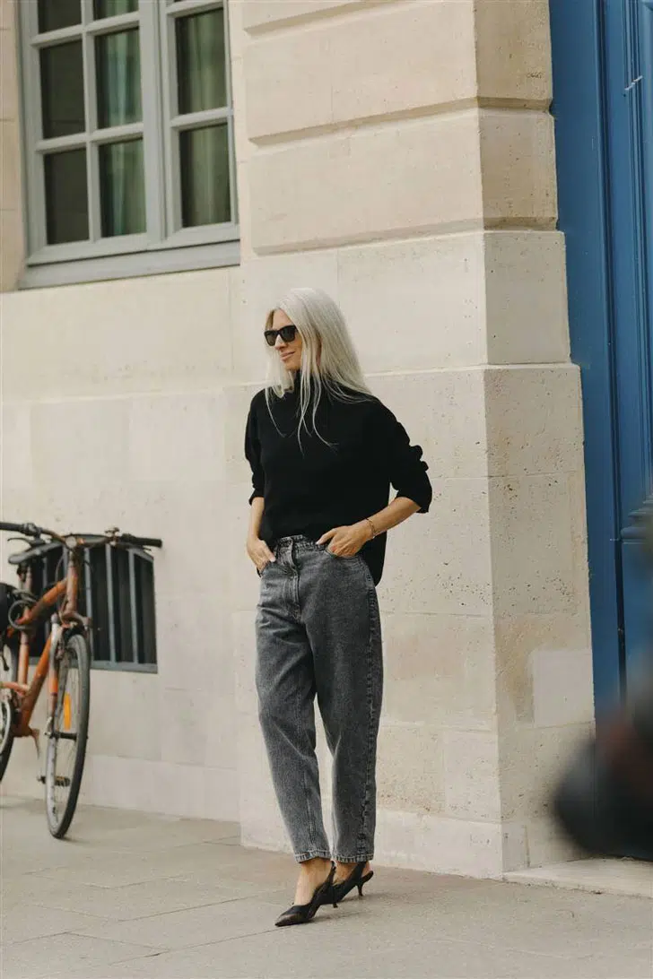 Женщина в серых джинсах, черном свитере и туфлях с ремешком на пятке