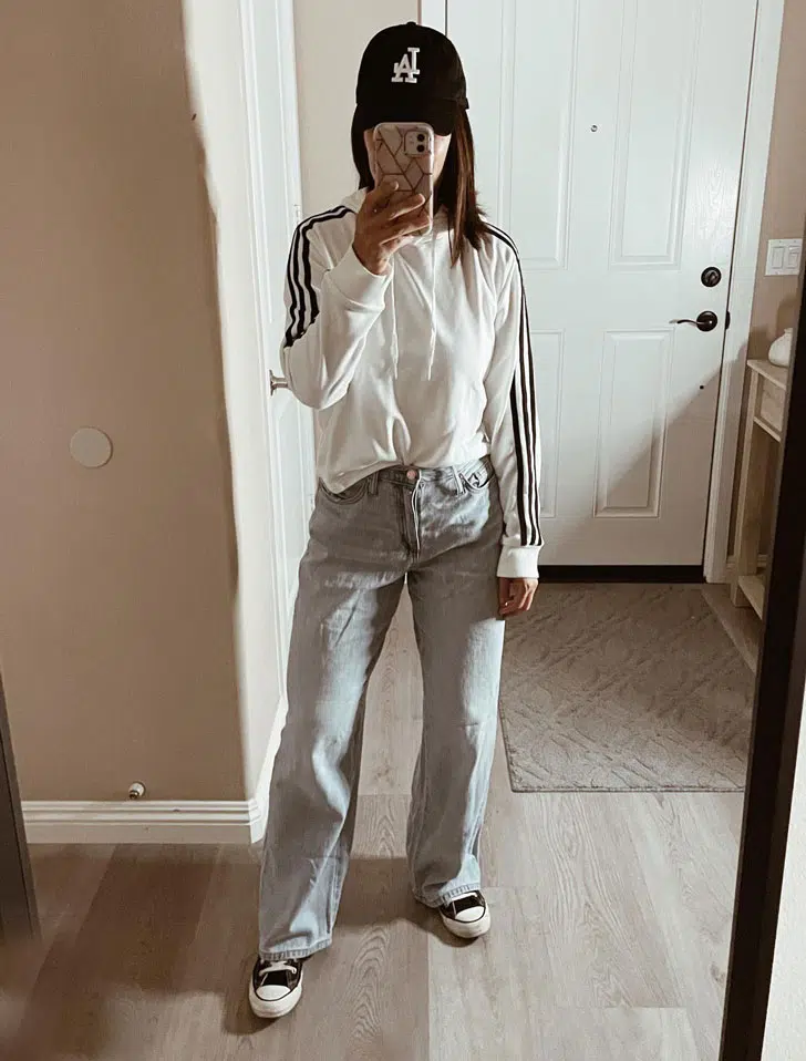 Девушка в свободных джинсах, белой спортивной кофте и ретро кроссовках