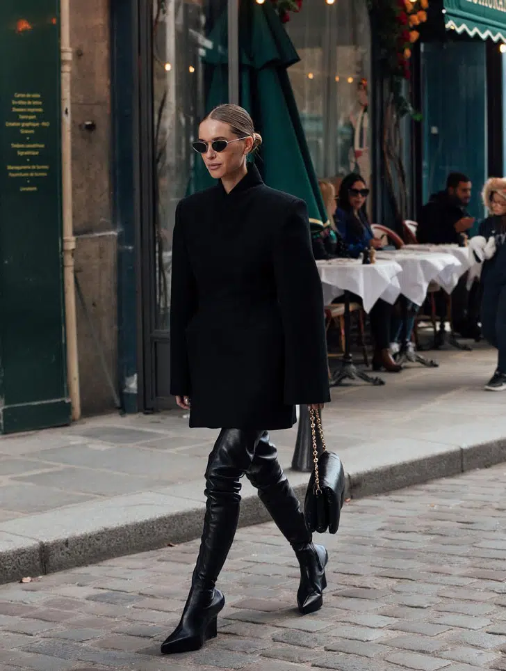 Девушка в черном пальто оверсайз и высоких кожаных ботфортах на модном и удобном каблуке