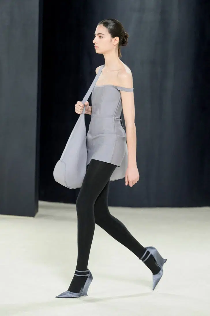 Модель в сером мини платье, огромной сумкой и туфлях с ремешками и модным каблуком