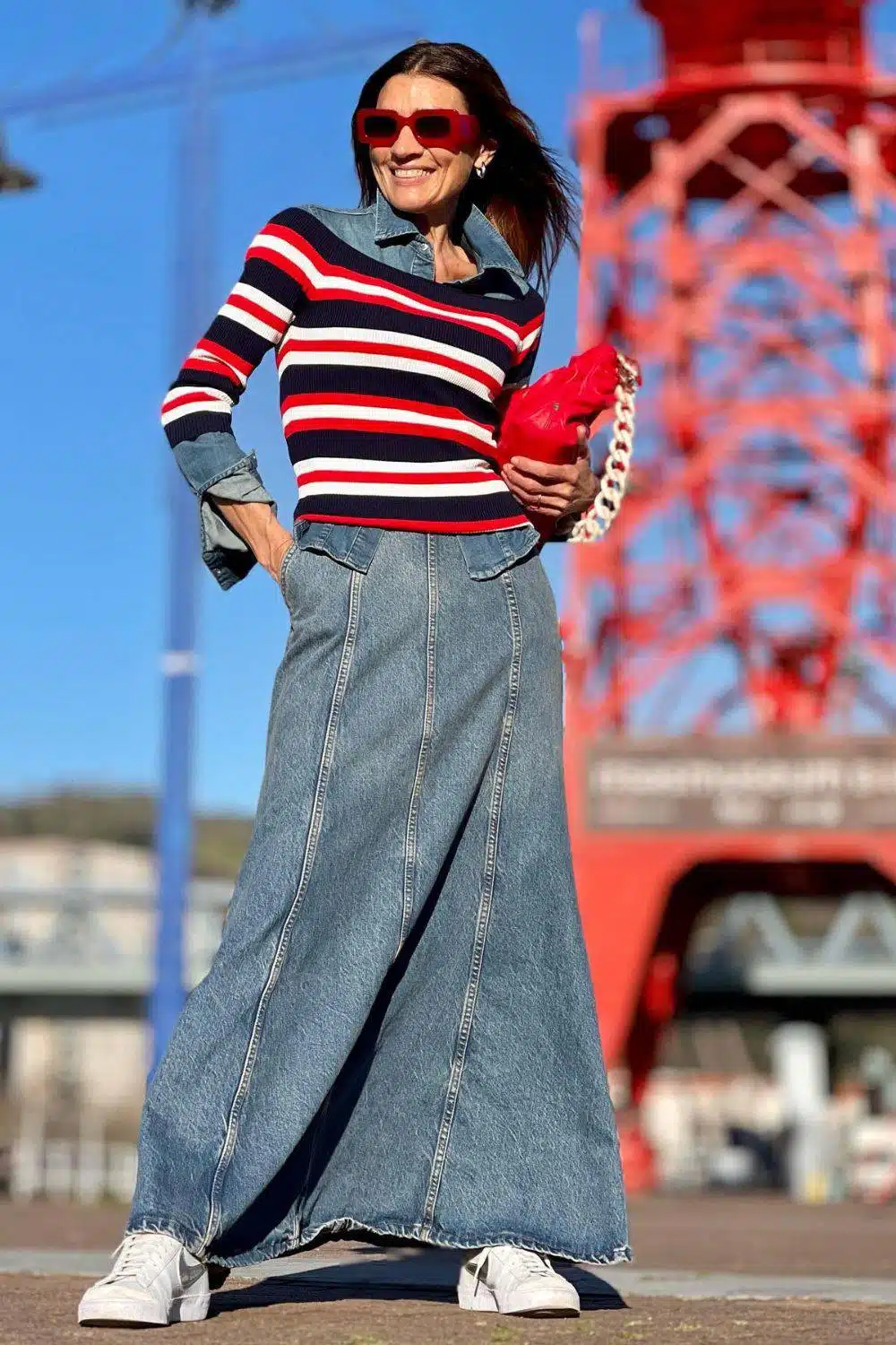 Женщина в джинсовой юбке макси, ярком свитере в полоску и кроссовках