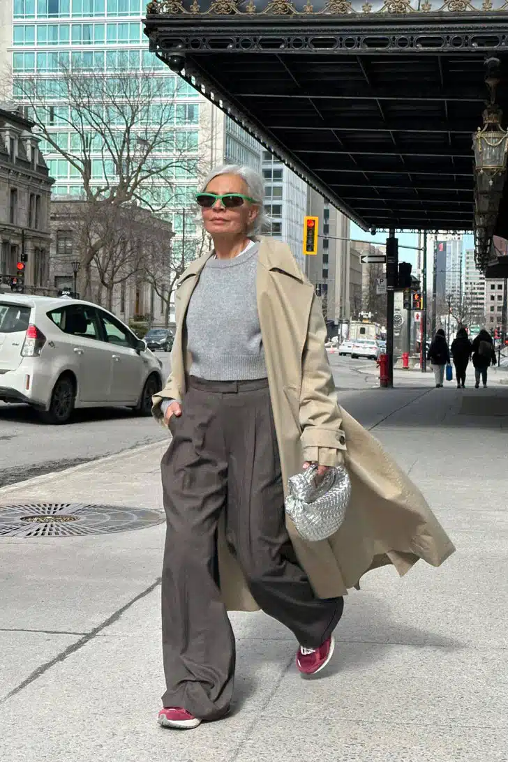 Грес Ганем в широких серых брюках, классическом плаще и бордовых кроссовках