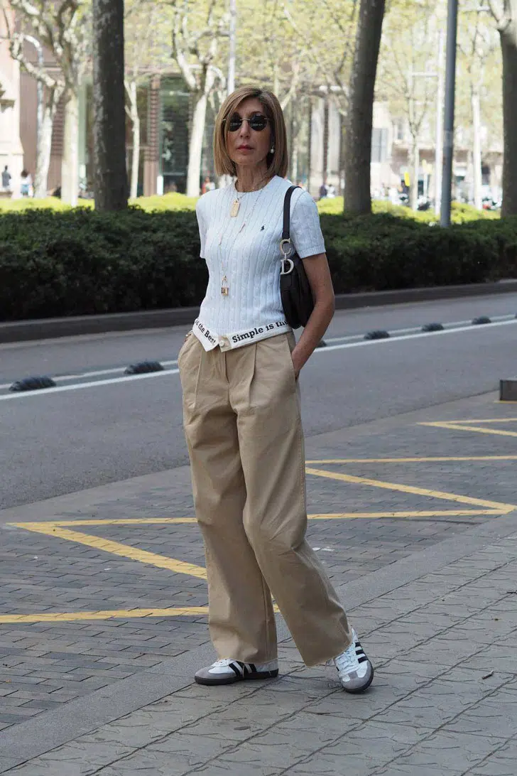 Женщина в брюках со складками, белой кофточке и кроссовках