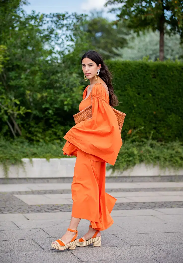 Девушка в оранжевом платье с широкими рукавами и босоножках с плетенной подошвой