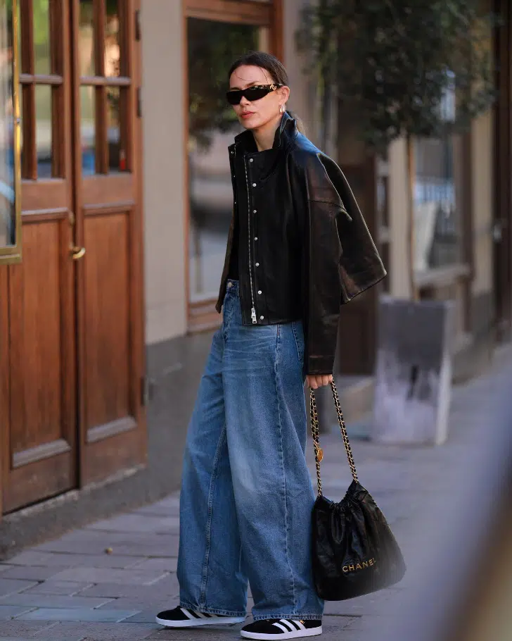Девушка в широких джинсах, кожаной куртке и простых черных кедах