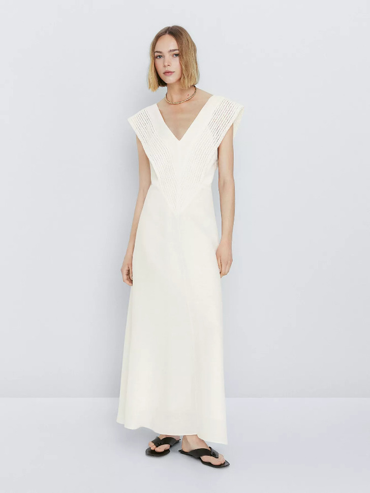 Модель в белом длинном платье с V образным вырезом без рукавов