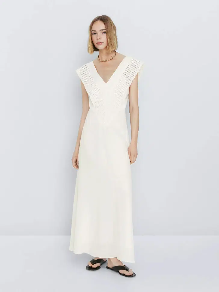 Модель в белом длинном платье с V образным вырезом без рукавов