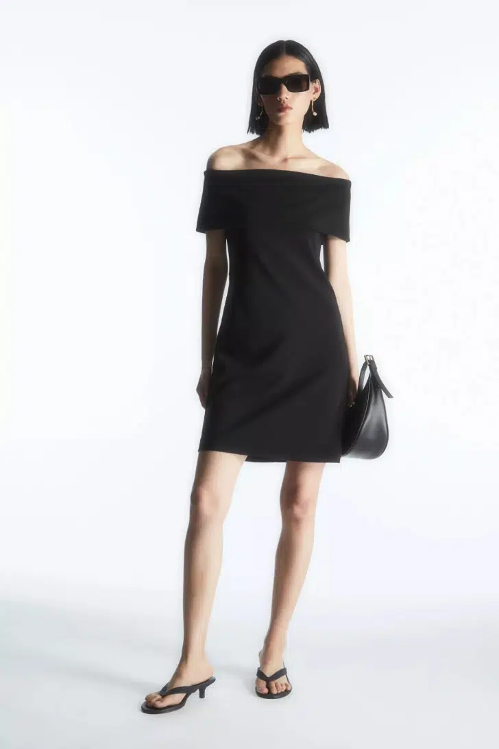 Модель в черном мини платье с открытыми плечами и черных босоножках