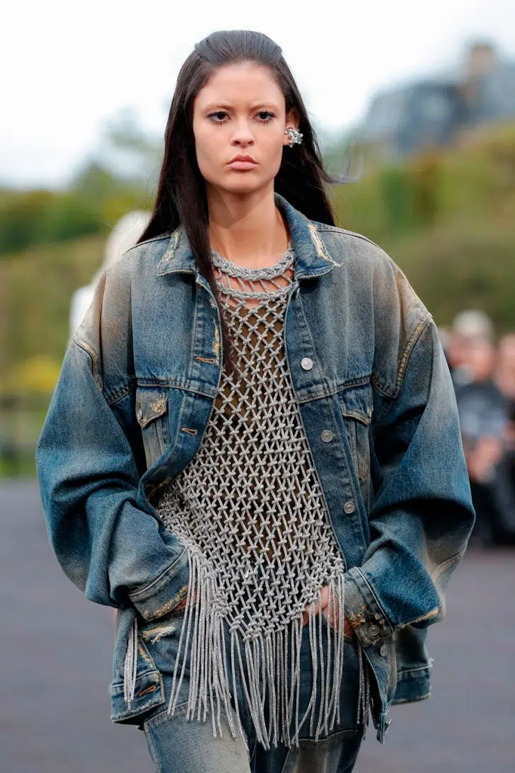 Модель в вязаном топе, джинсовке оверсайз и серебряных украшениях от Givenchy