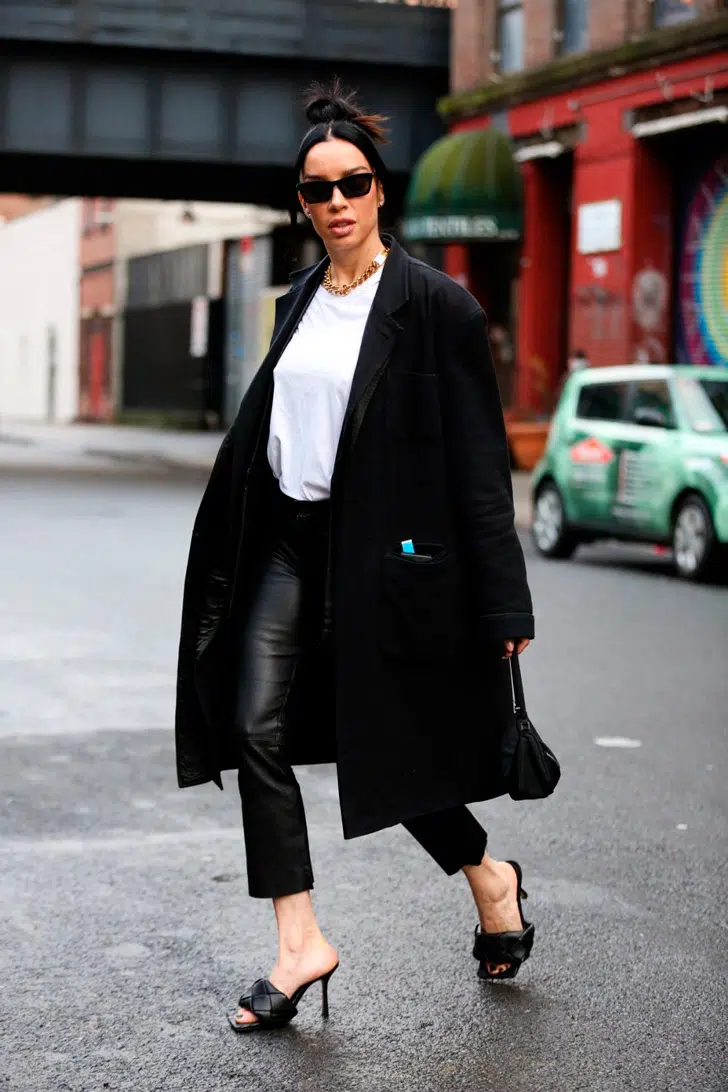 Девушка в кожаных брюках, черном пальто и босоножках на каблуке без задника