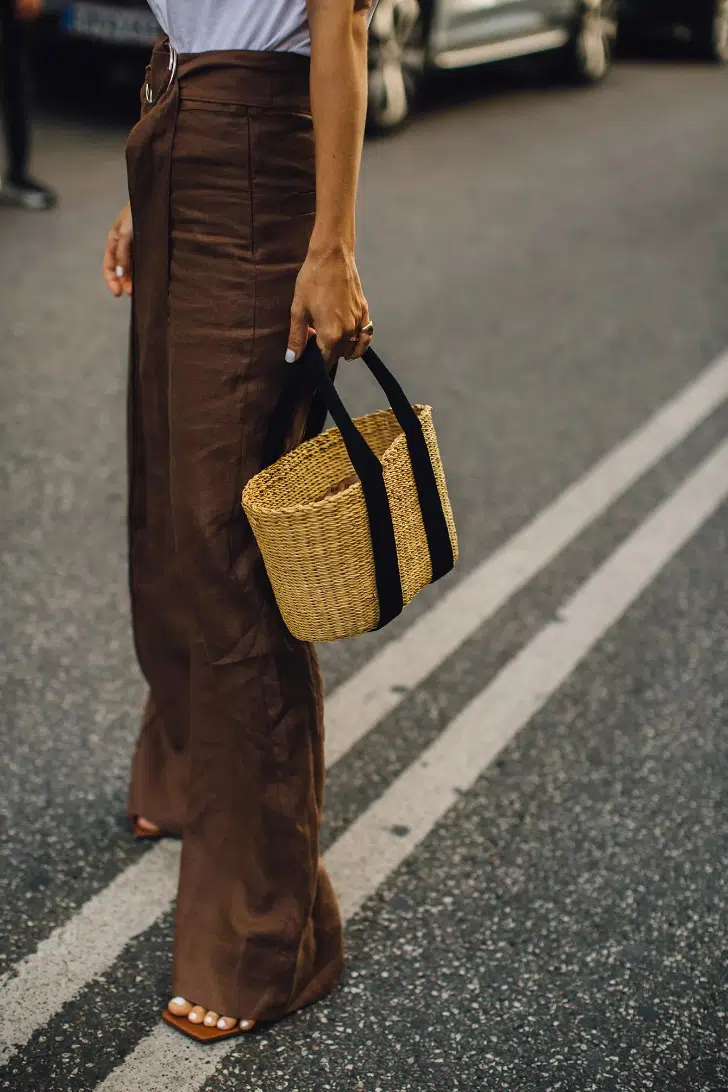 Девушка в свободных коричневых брюках, белой футболке и с небольшой сумкой-корзиной