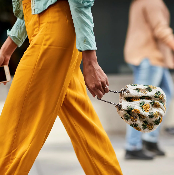 Девушка в свободных оранжевых брюках и с небольшой мягкой сумочкой с принтом