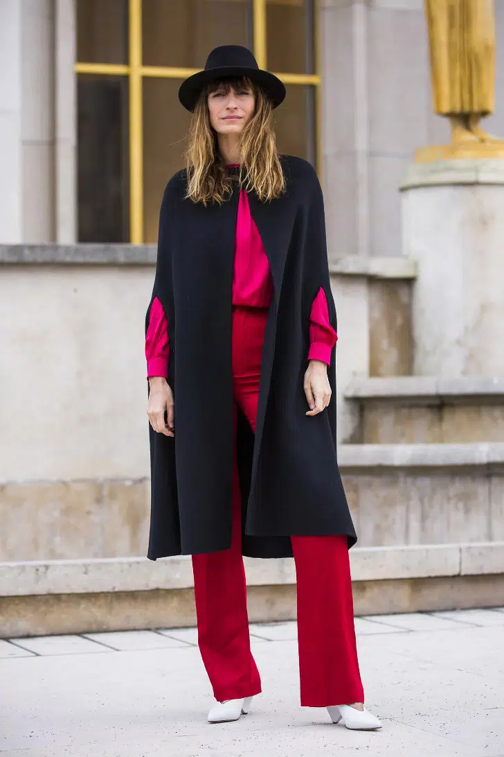 Кэролайн Де Мегре в красных брюках, атласной блузке и черной накидке