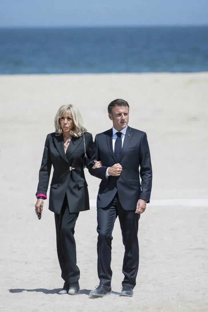 Брижит Макрон в черном костюме с закатанными рукавами прогуливается по пляжу