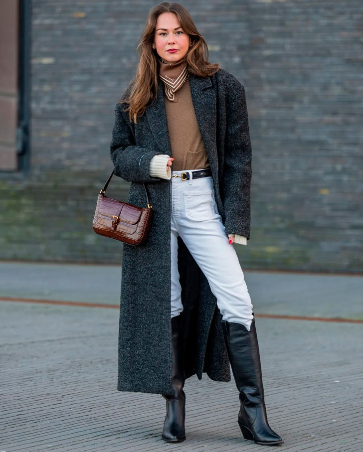 Девушка в светлых джинсах с ремнем, сером классическом пальто и ковбойских сапогах