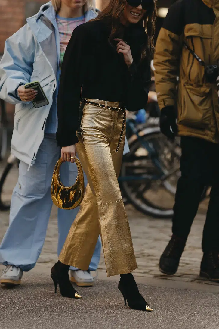 Девушка в золотых металлизированных брюках, черном свитере и туфлях на шпильке
