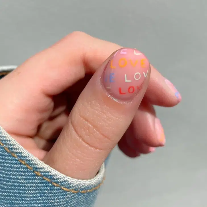 Нейтральный маникюр с разноцветными надписями на коротких ногтях
