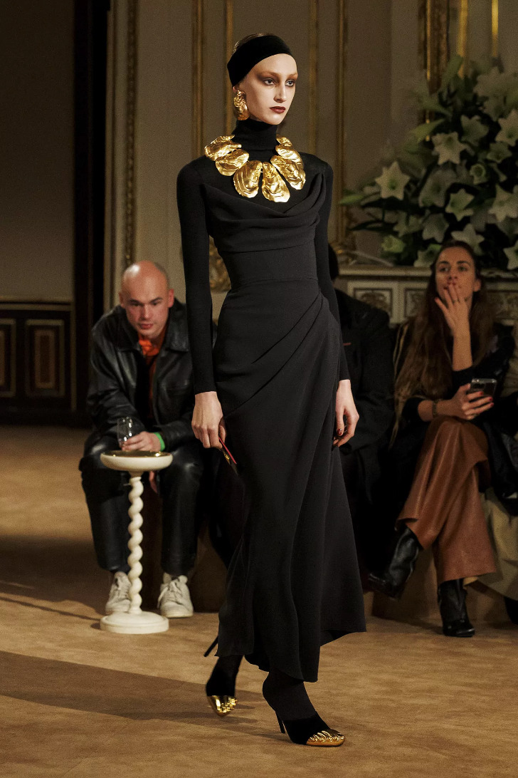 Модель в черном макси платье с длинными рукавами и с золотыми объемными аксессуарами