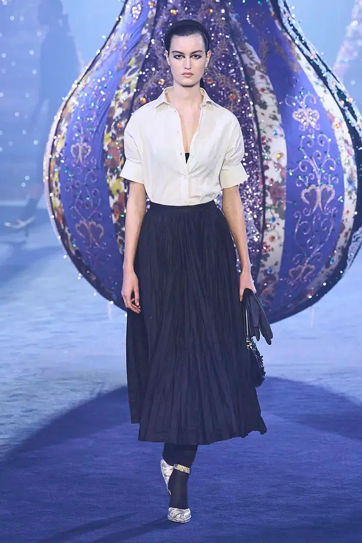 Модель в длинной плиссированной юбке, белой рубашке и туфлях от Dior