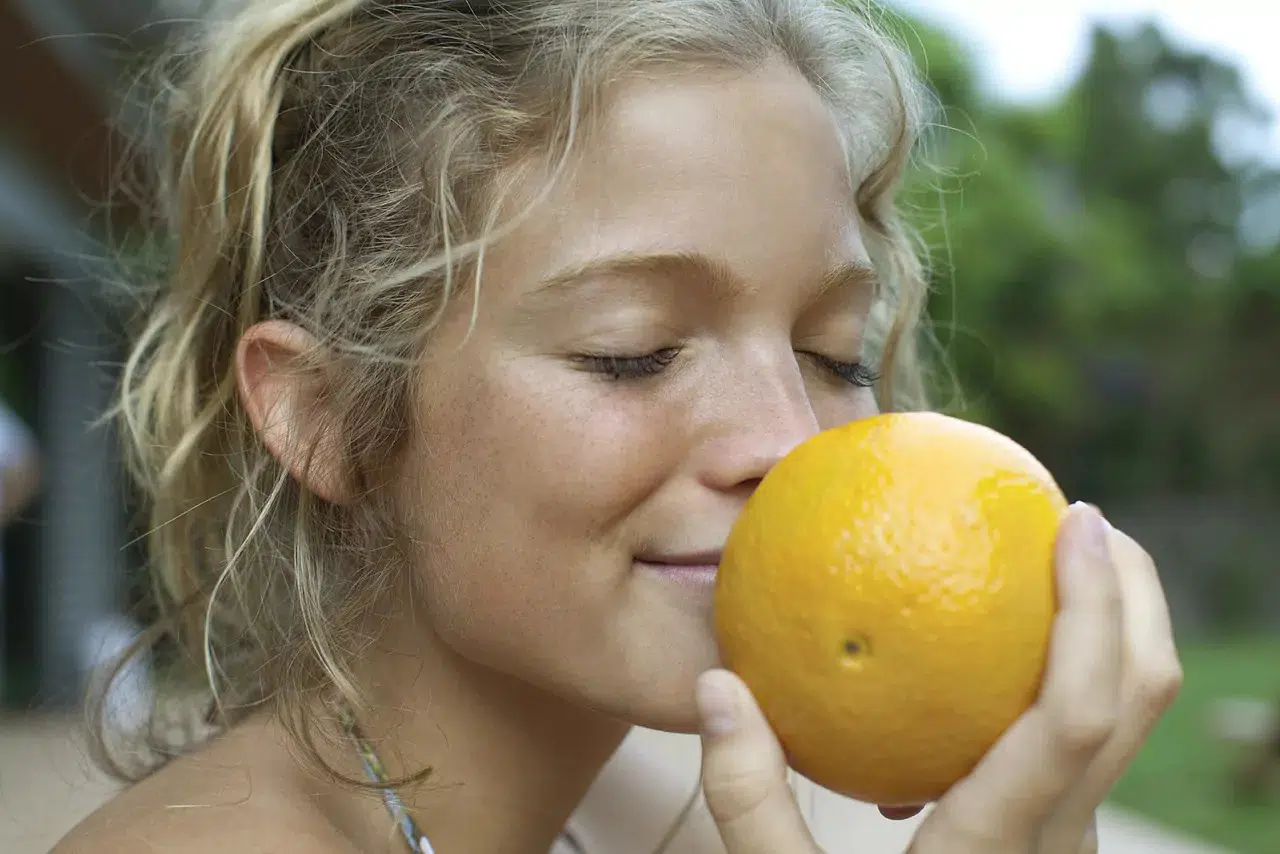 Девушка с русыми волосами нюхает апельсин
