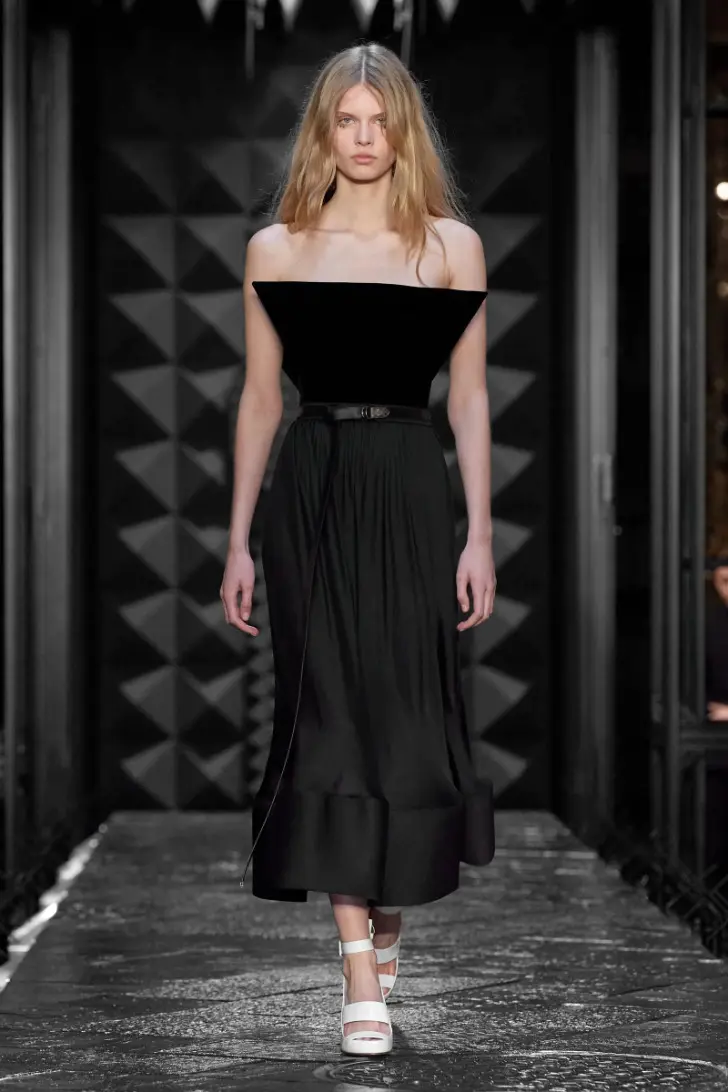 Модель в черном платье миди с оригинальным верхом и белых босоножках от louis vuitton