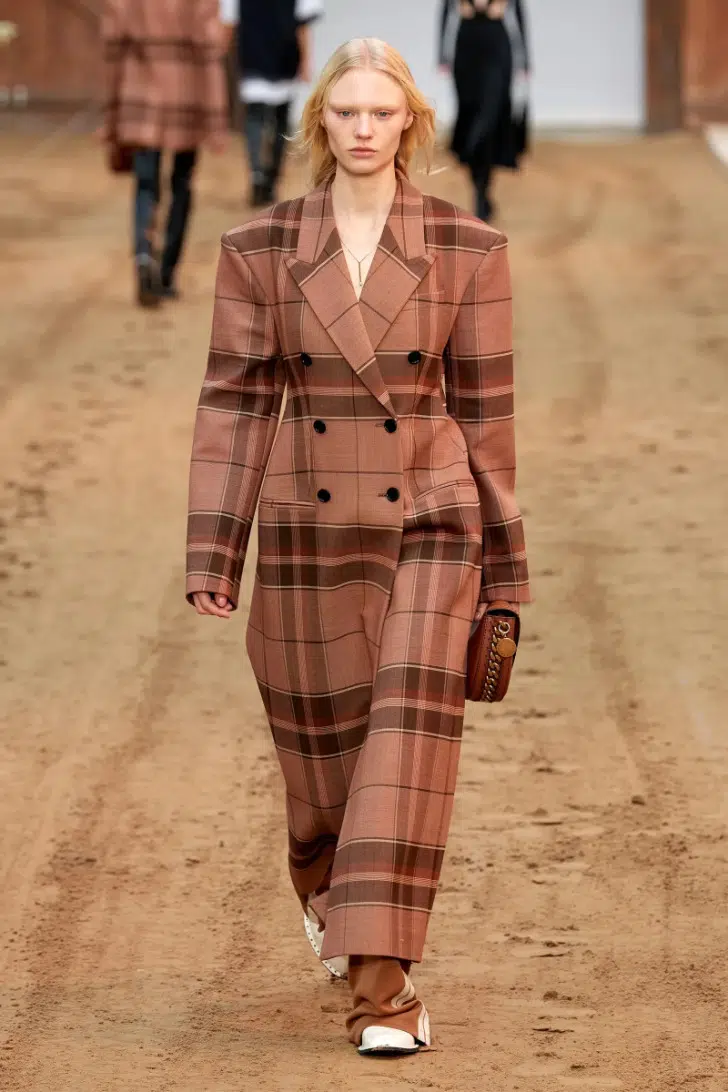 Модель в коричневом длинном пальто в клетку в стиле оверсайз от Stella McCartney