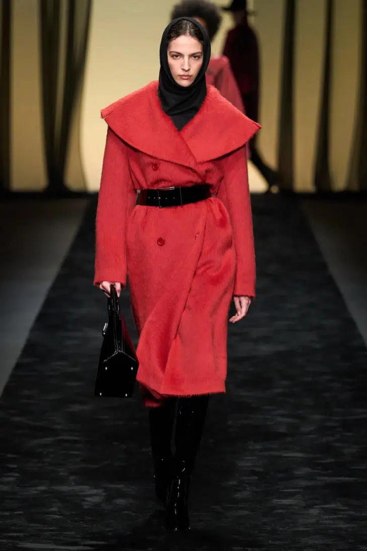 Модель в красном пальто миди с черным ремнем и большим воротником от Alberta Ferretti