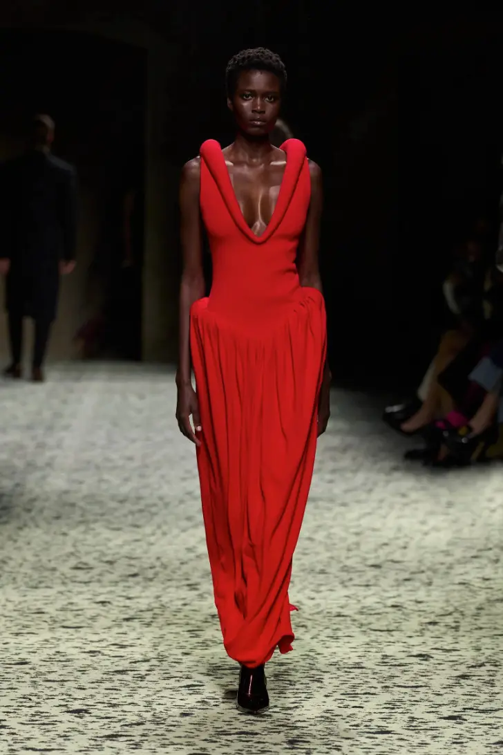Модель в красном вечернем платье макси без рукавов и глубоким декольте от bottega veneta