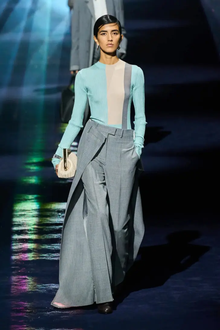 Модель в серых классических брюках с юбкой и голубой водолазке от fendi