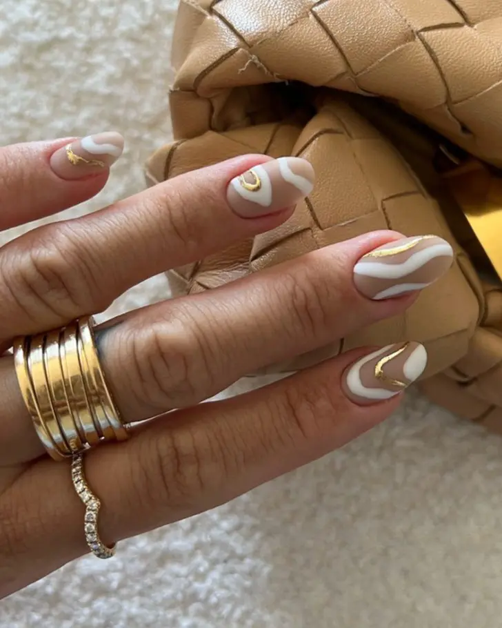 Нейтральный маникюр с белыми и золотыми линиями на овальных ногтях