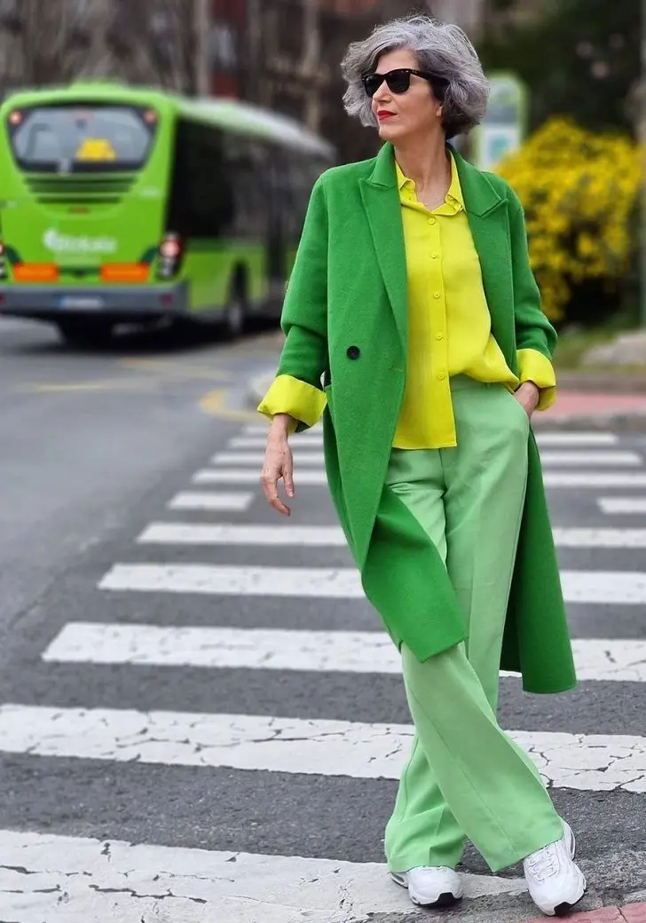 Женщина в зеленых брюках, желтой рубашке и белых кроссовках