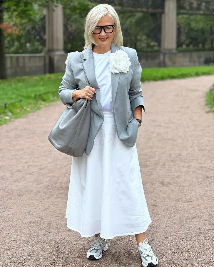 Женщина в белой А-образной юбке, сером пиджаке и кроссовках