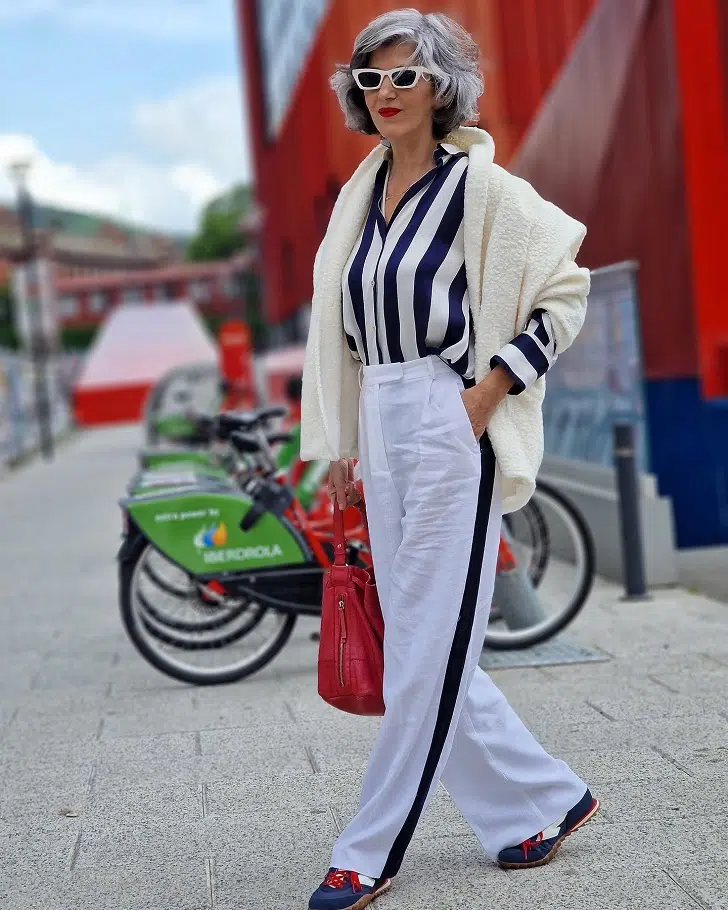 Женщина в белых брюках с лампасами, полосатой блузке и кроссовках