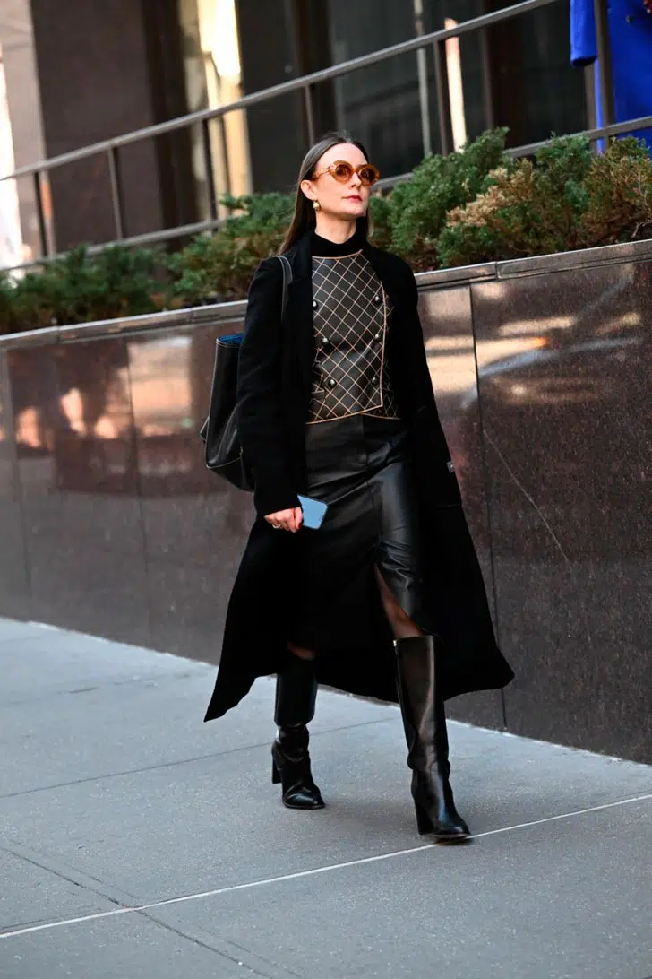 Девушка в кожаной юбке с разрезом, классическом черном пальто и высоких сапогах на каблуке