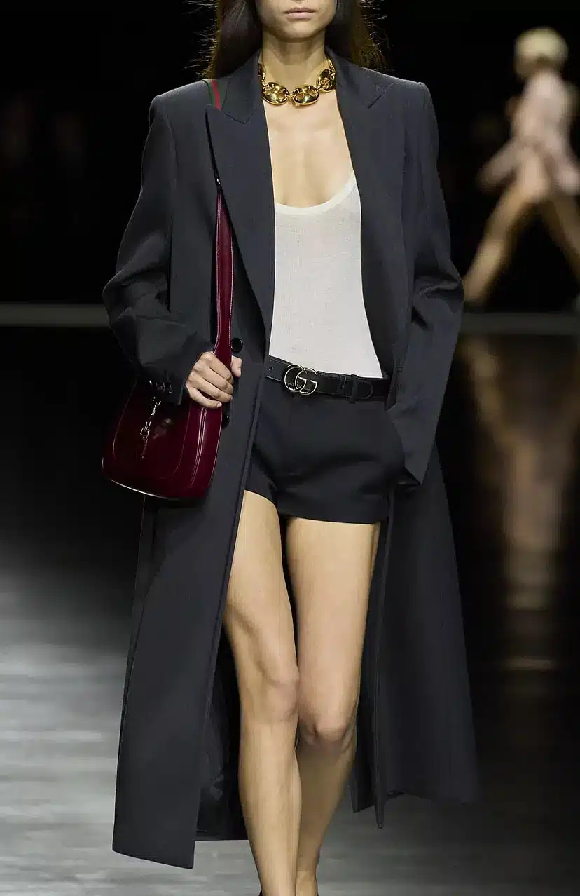 Модель в мини шортах с ремнем, топе и длинном классическом пальто