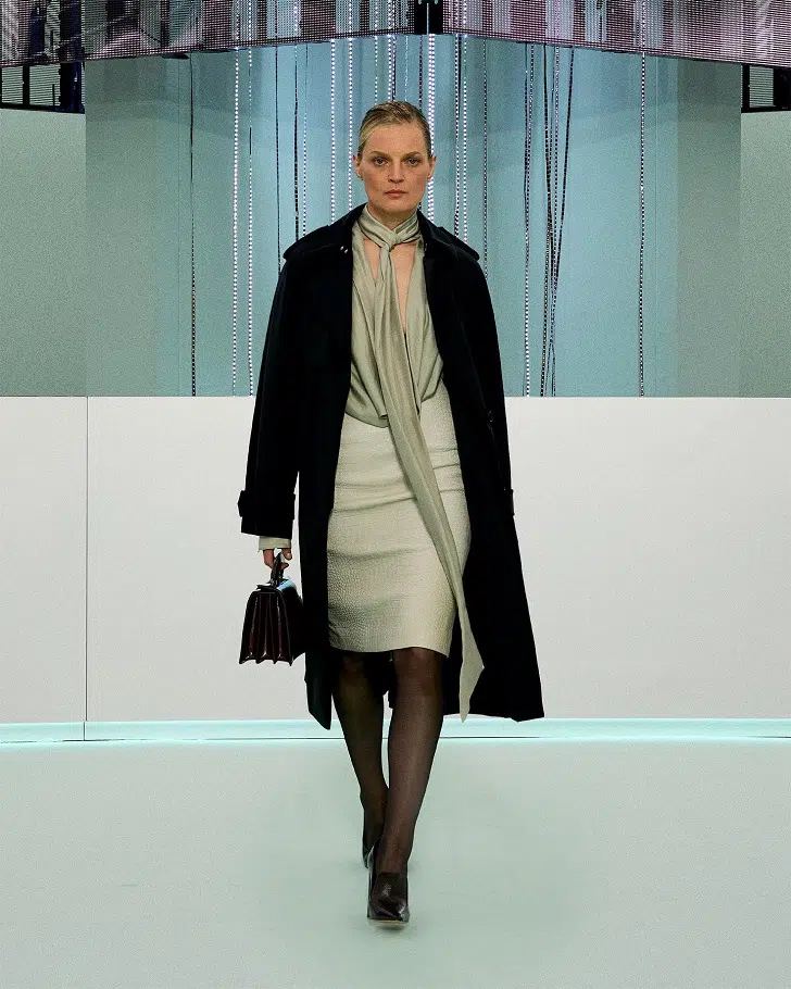 Модель в кожаной юбке, шелковой блузке и черное пальто длины миди