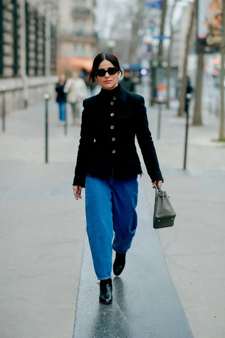Девушка в классических синих джинсах, черном жакете и ботильонах
