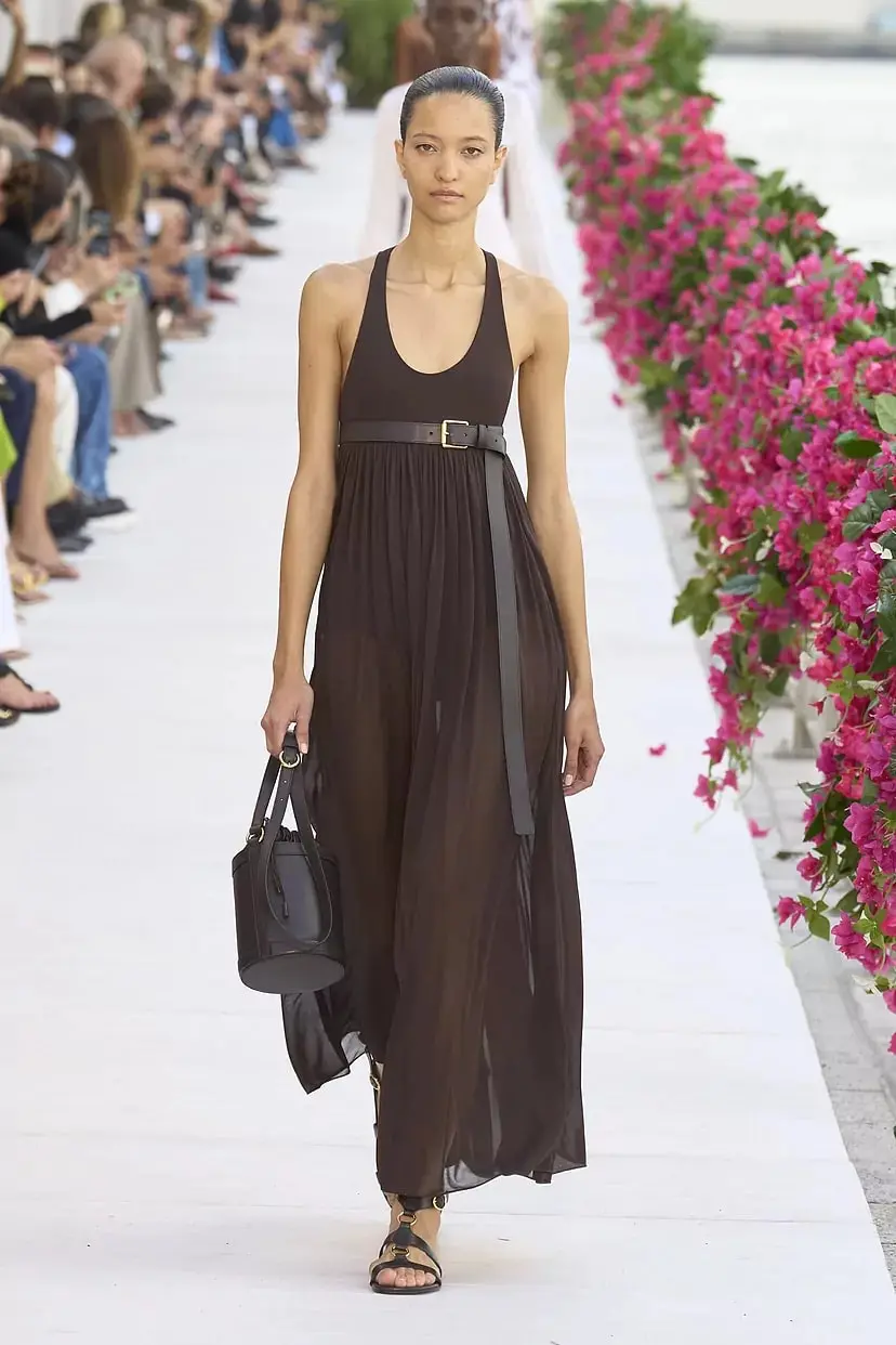 Модель в коричневом платье миди и черных сандалиях от Michael Kors