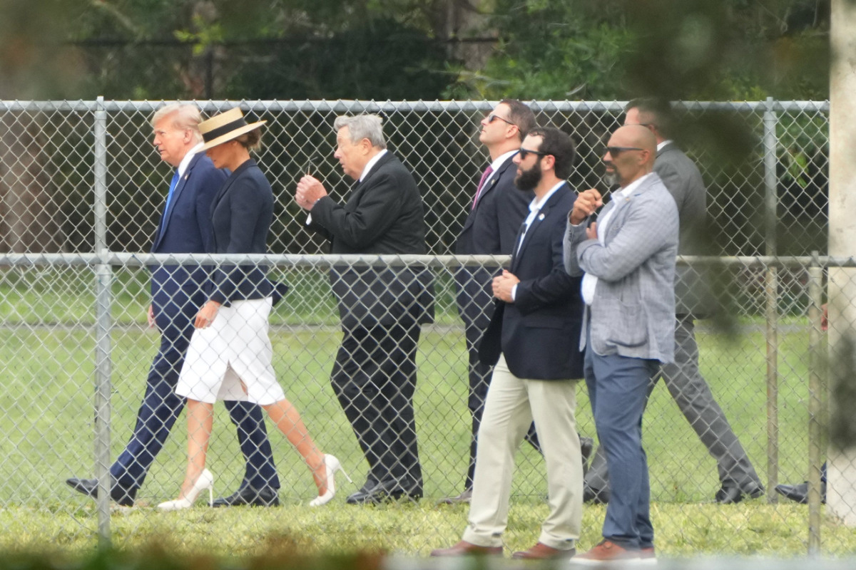 Мелания Трамп в белых туфлях, юбке и черном жакете идет на выпускной сына